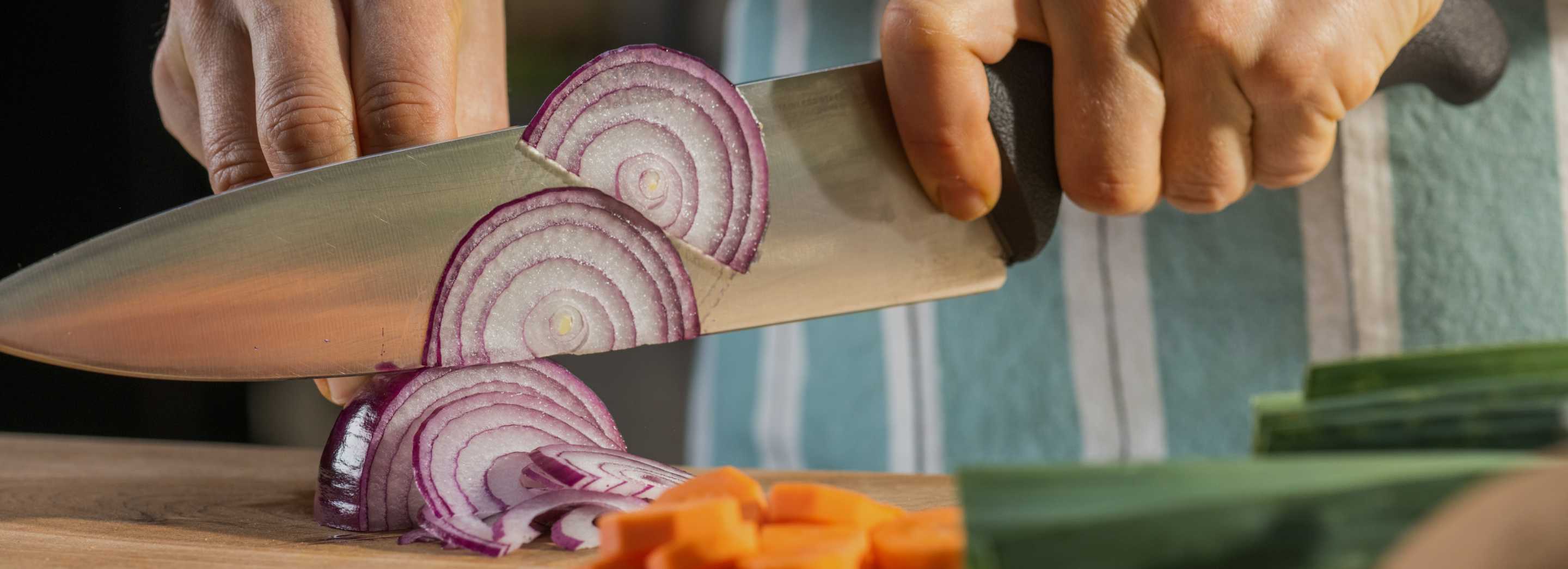 A person's hand is shown slicing an onion with a large bladed knife.