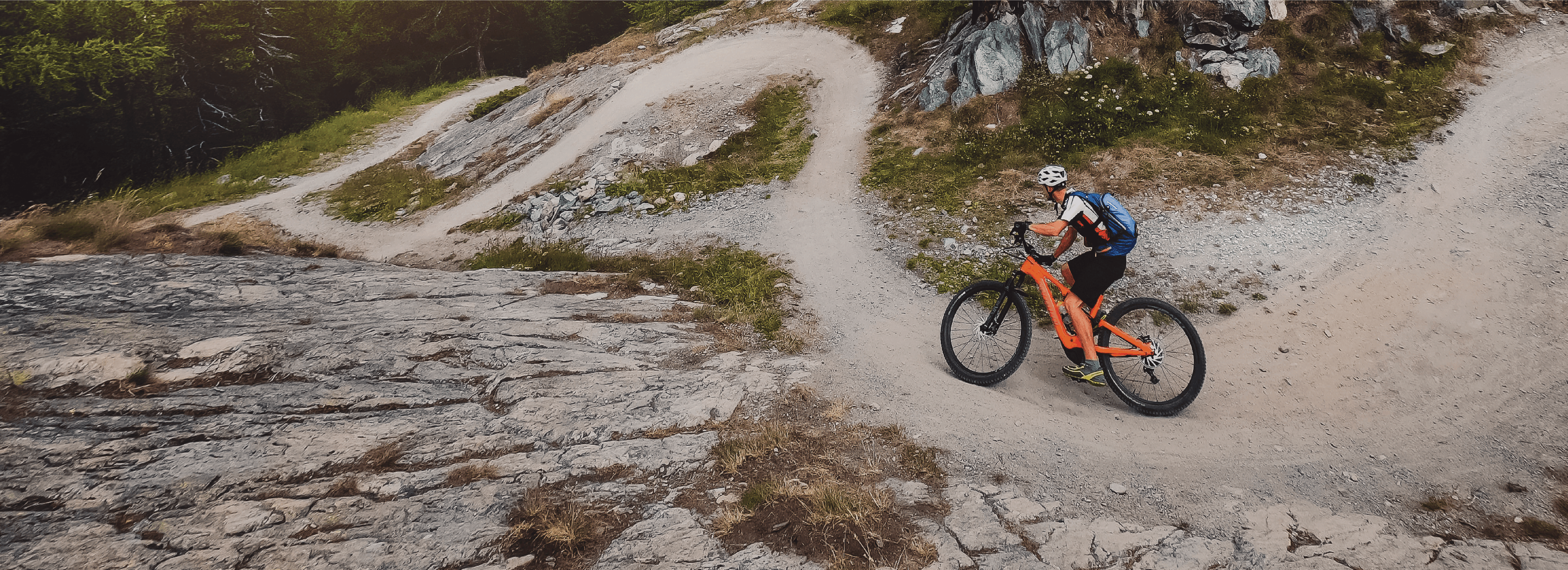 A man rides his orange mountain bike down a dirt trail.