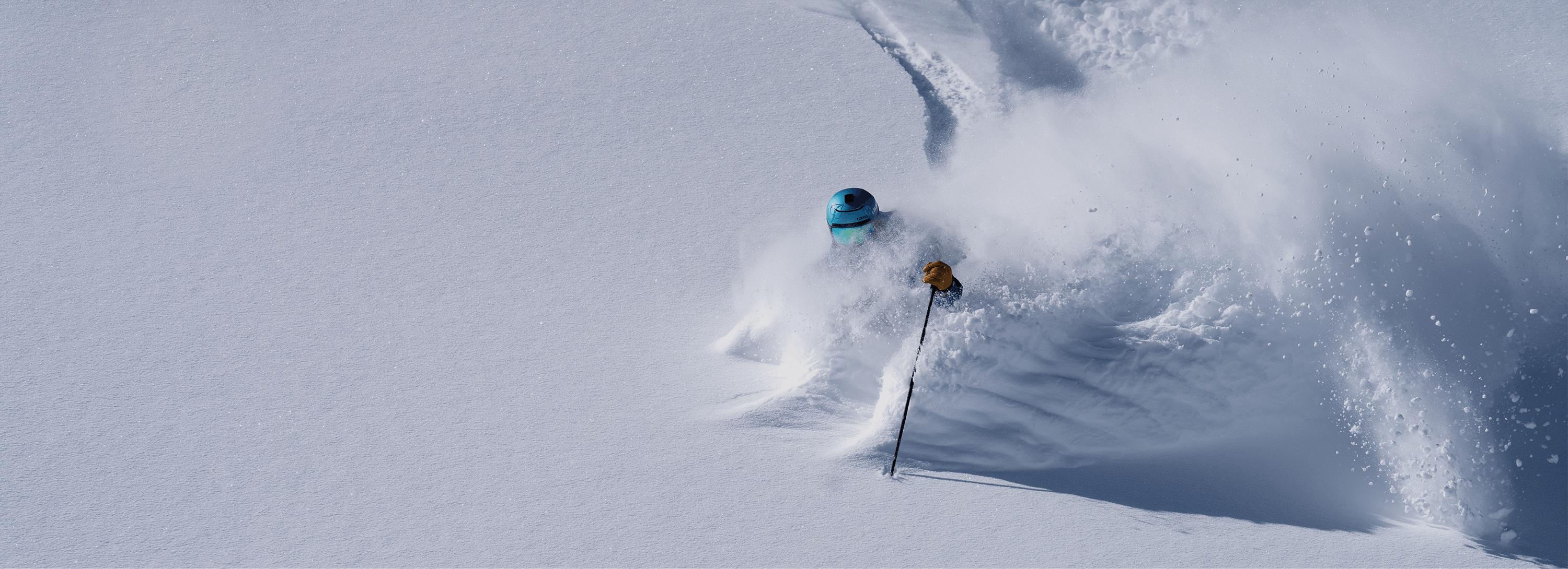 A skier leaves a plume of snow behind their wake as they shred down a mountainside. 