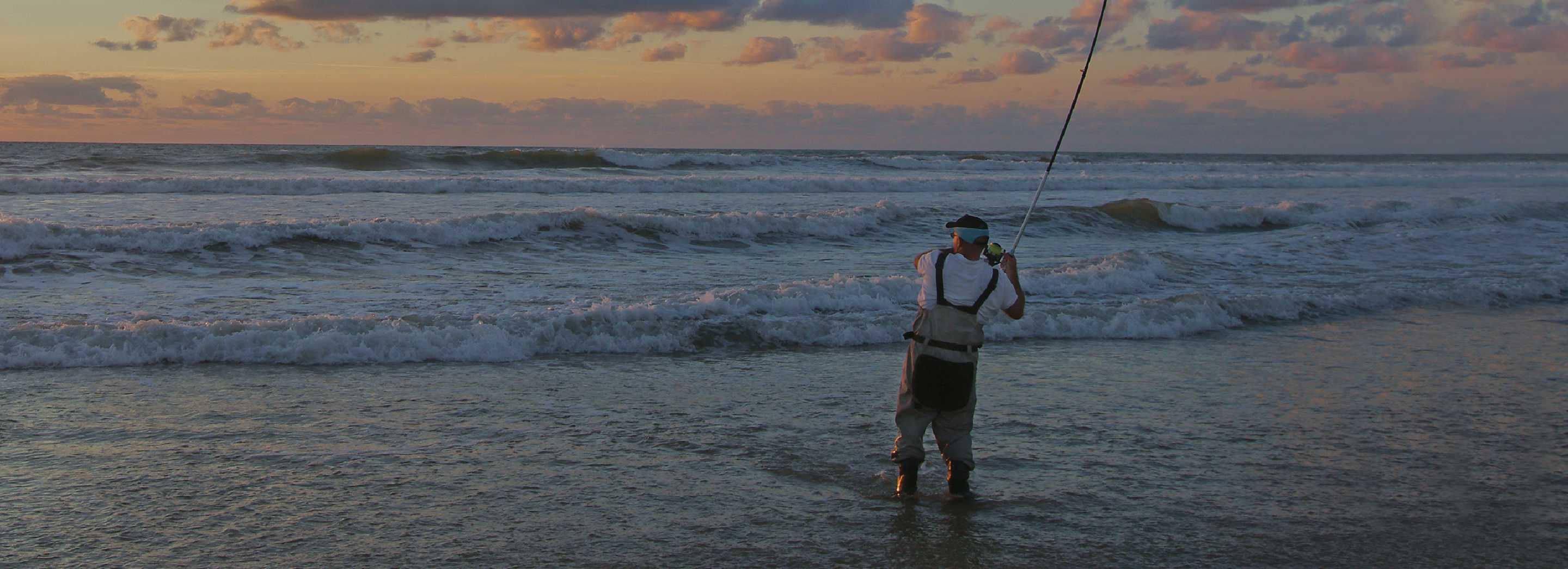 A man prepares to cast his reel into the ocean as the sun sets. 